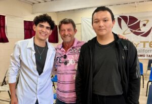 Oswaldo and Christian stand with Baja Angels of the Sea founder Bruno, smiling together inside the high school auditorium following the Rotary Scholars scholarship presentation in Baja California